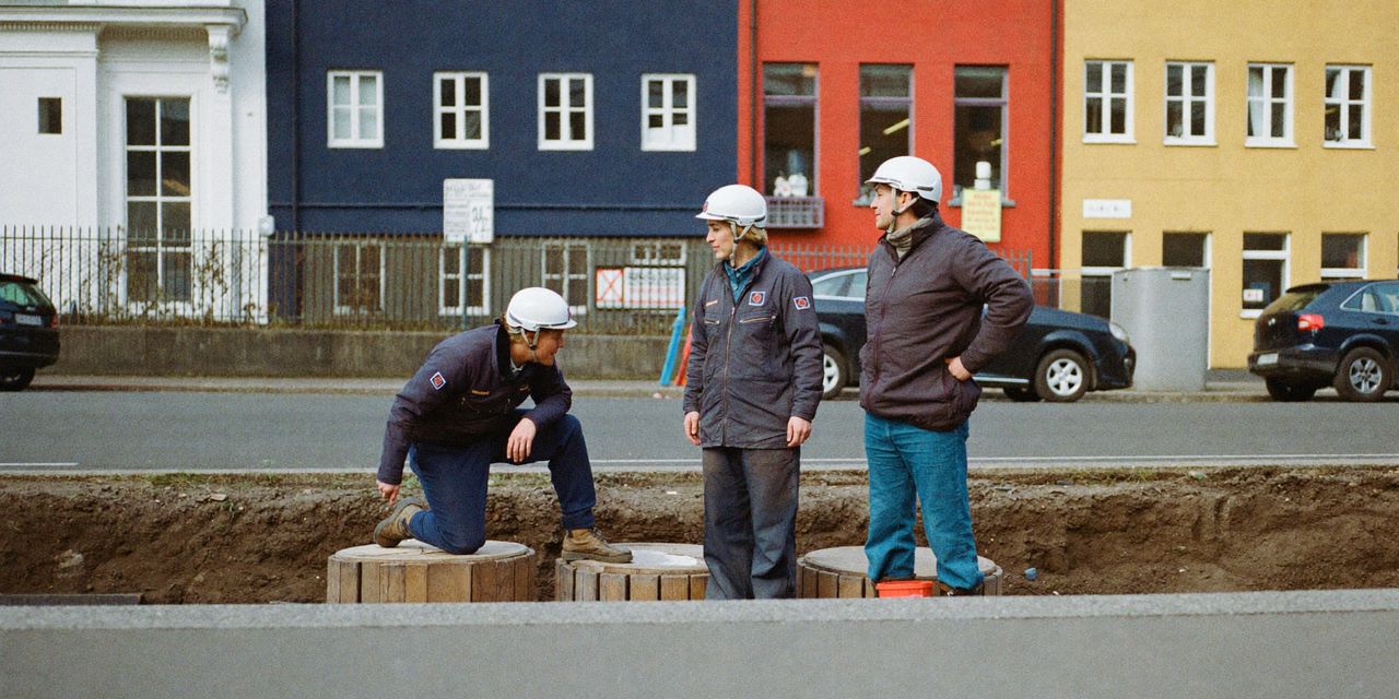 Kabelmonteure mit Helm an einem offenen Graben in der Straße, mit Kabeltrommeln