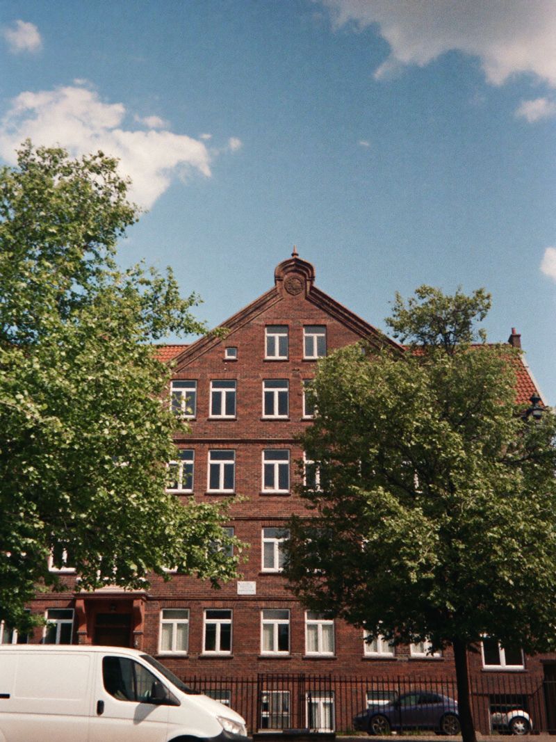 Wohnhaus aus rotem Backstein in einer Straße mit Bäumen, davor ein weißer Transporter
